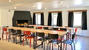 Een vergaderruimte met een lange tafel en stoelen, een open haard en ramen voorzien van gordijnen.