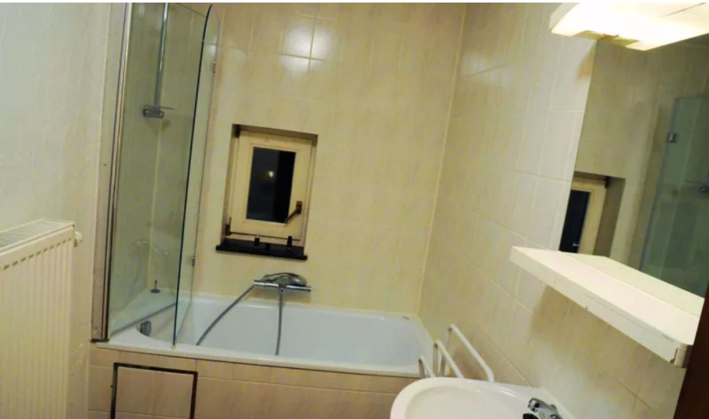 Een badkamer met een bad, een klein raam, een spiegel en een wit wastafel.