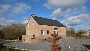 A brick building with a sloped roof, a large window, and a circular driveway. - Holiday Home in Ardennes With Bubble Bath (Somme-Leuze)