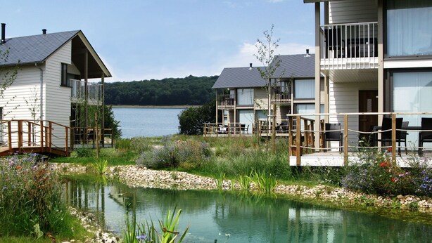 Une propriété au bord du lac, dotée d’un petit étang, d’une terrasse en bois et d’un bâtiment avec un balcon donnant sur l’eau.