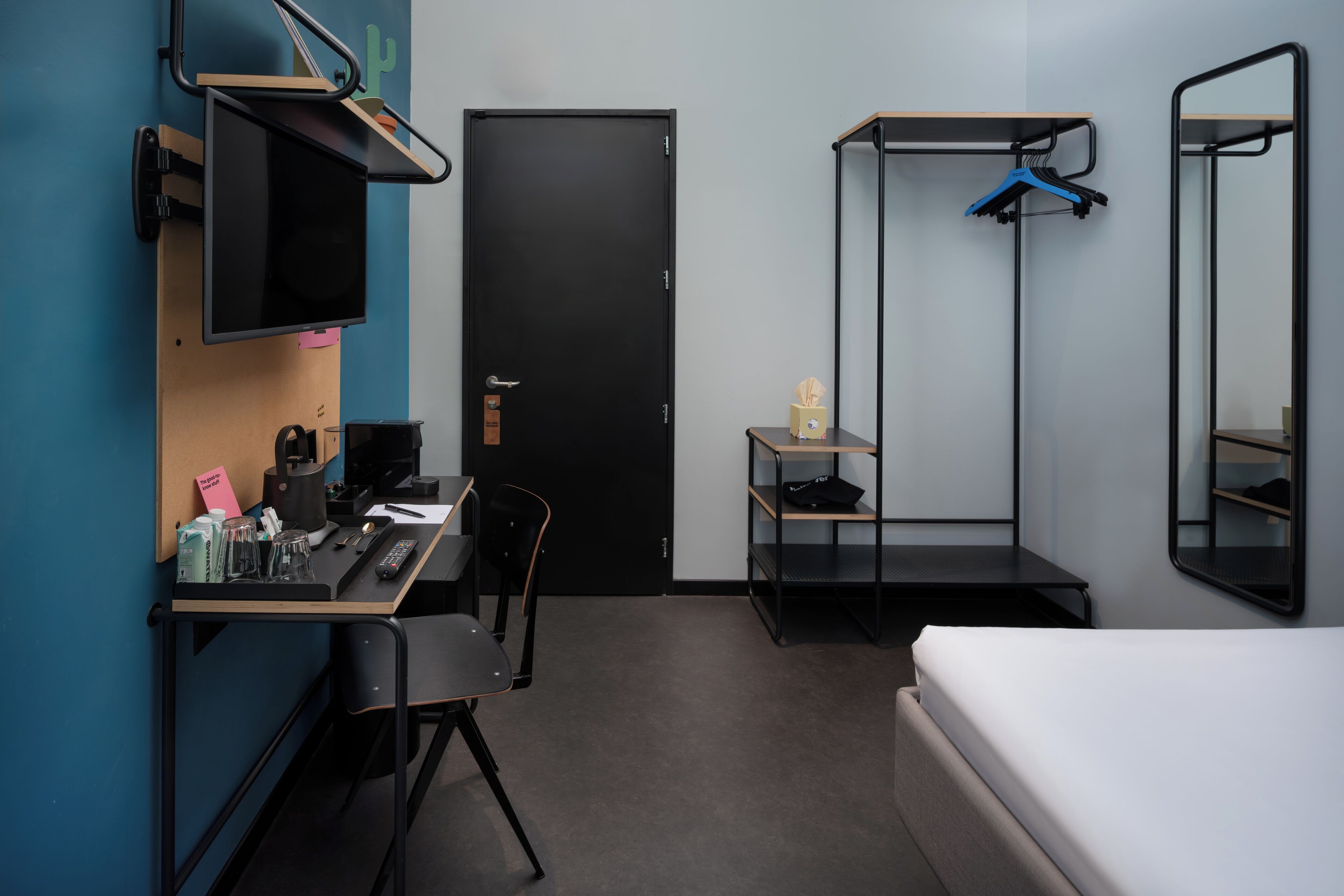 A compact hotel room with a desk, chair, bed, and a wardrobe with a mirror.