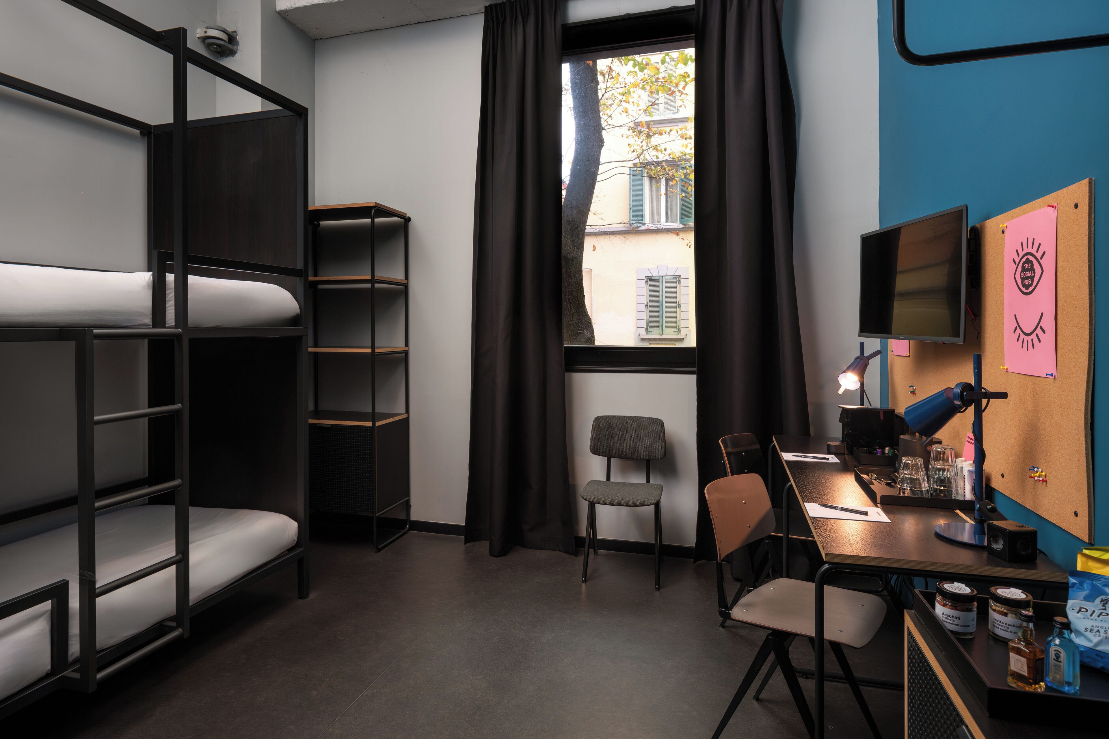 Habitación tipo dormitorio con literas, un escritorio, una silla, un monitor de computadora y una ventana con cortinas.