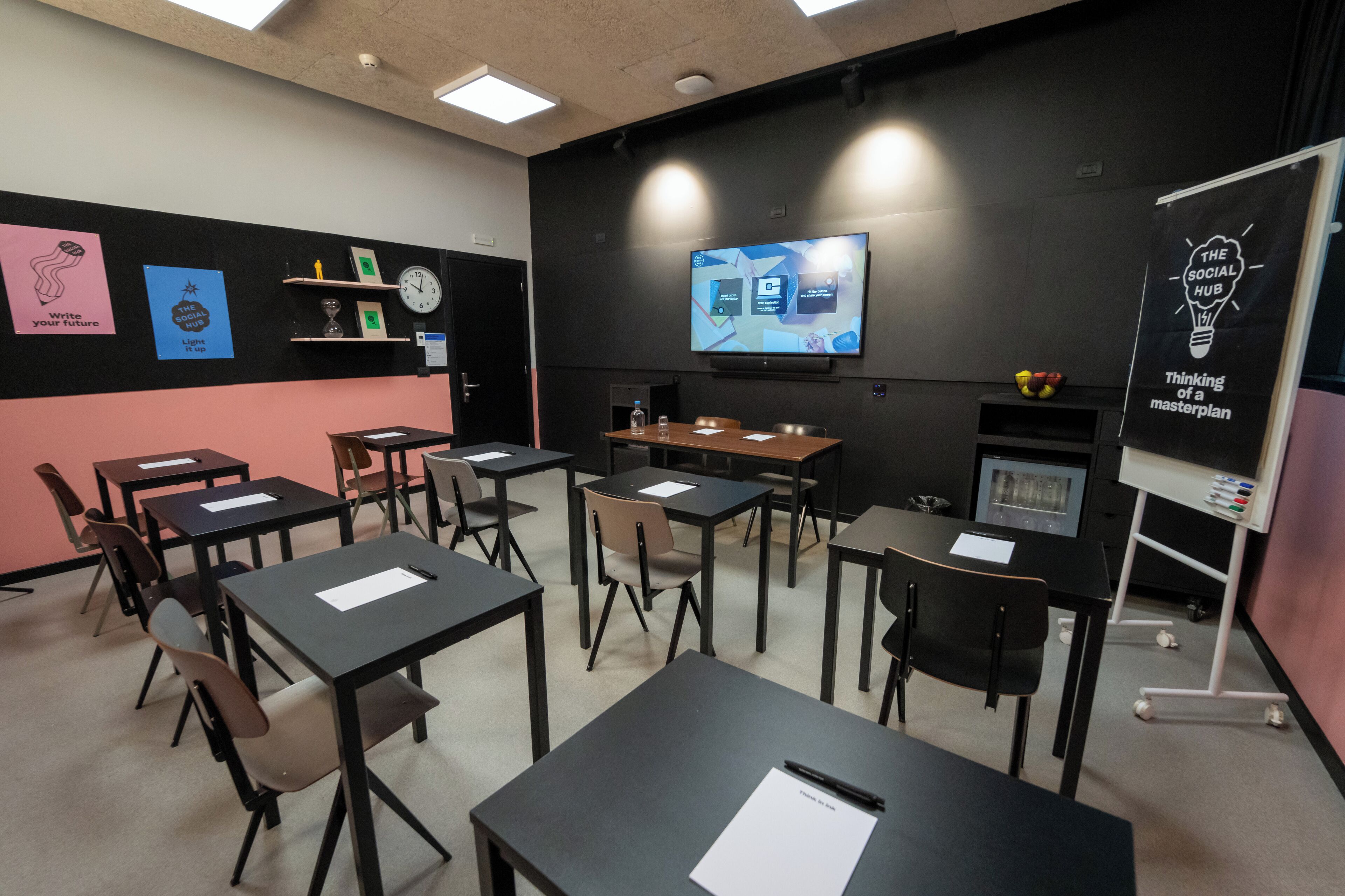 Un aula con pupitres, sillas, una pantalla de proyector y carteles educativos en las paredes.