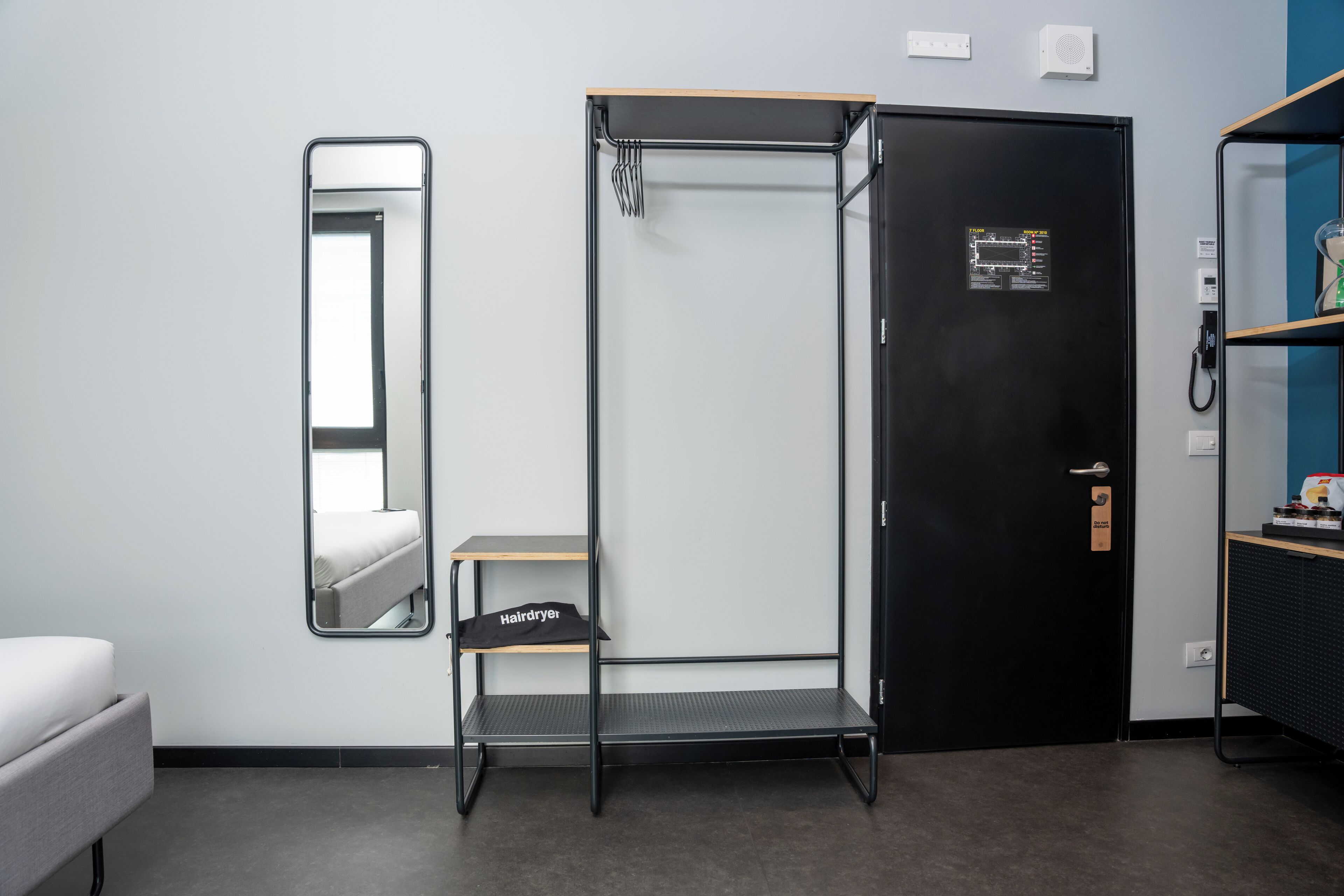 Una habitación compacta con cama, armario, espejo y un pequeño estante con secador de pelo.