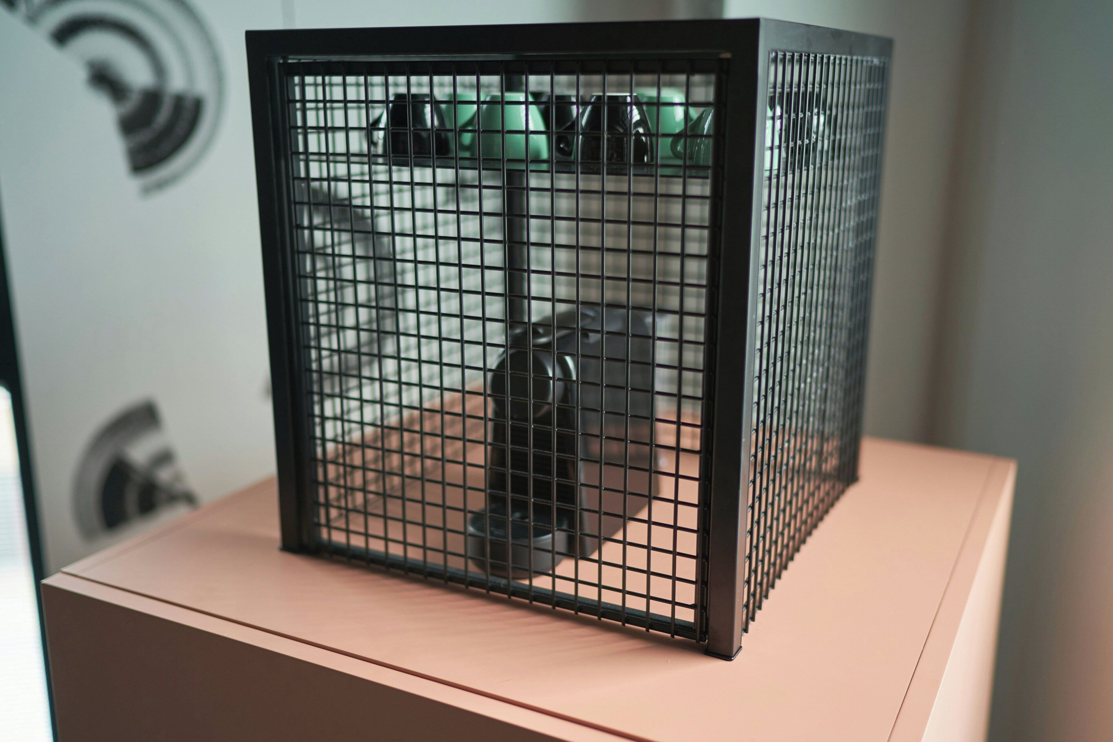 A black metal cage with a grid pattern, placed on a wooden surface.