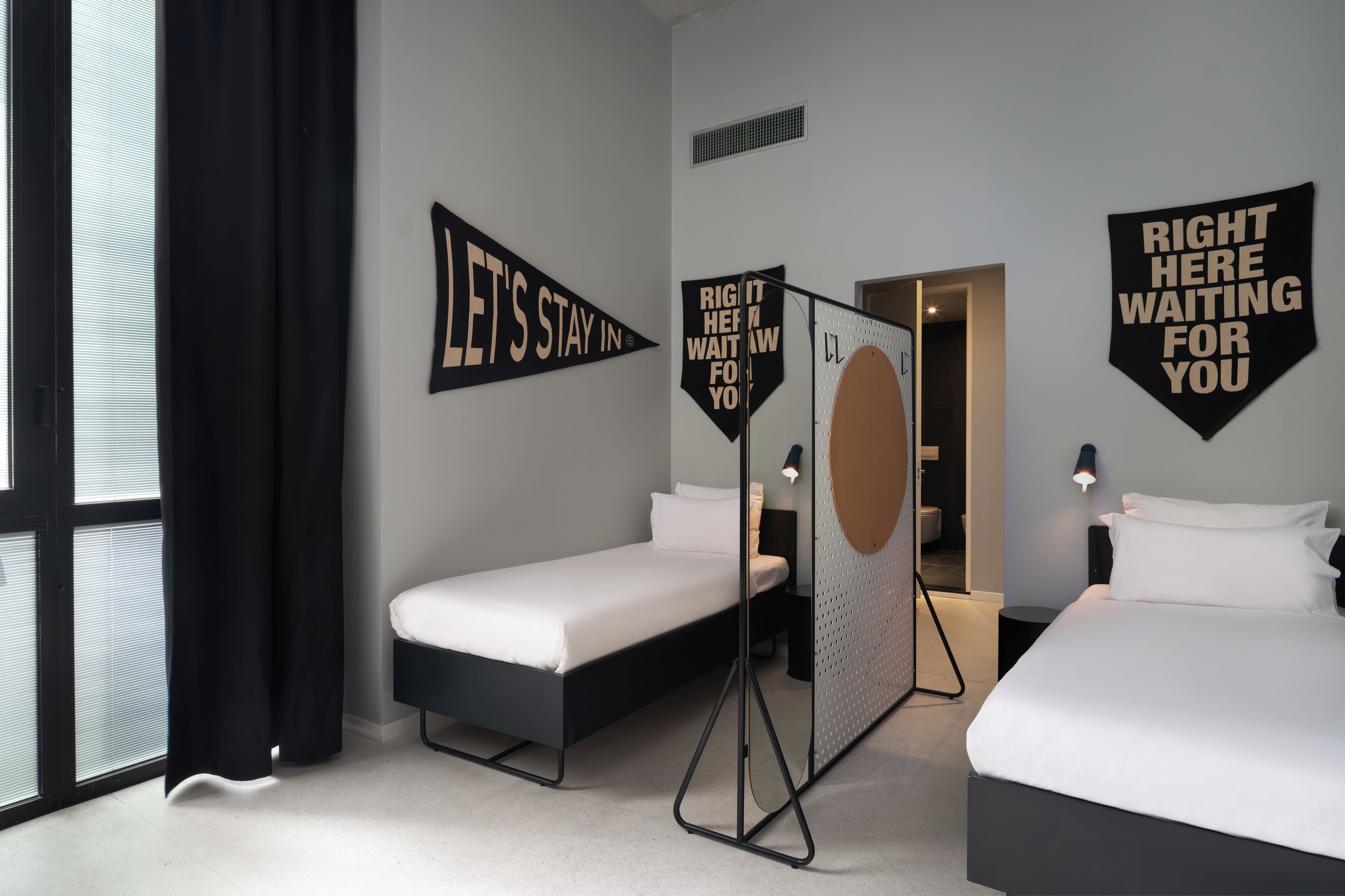 A hotel room with two beds, a window with black curtains, and motivational wall art.