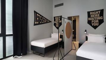 A hotel room with two beds, a window with black curtains, and motivational wall art.