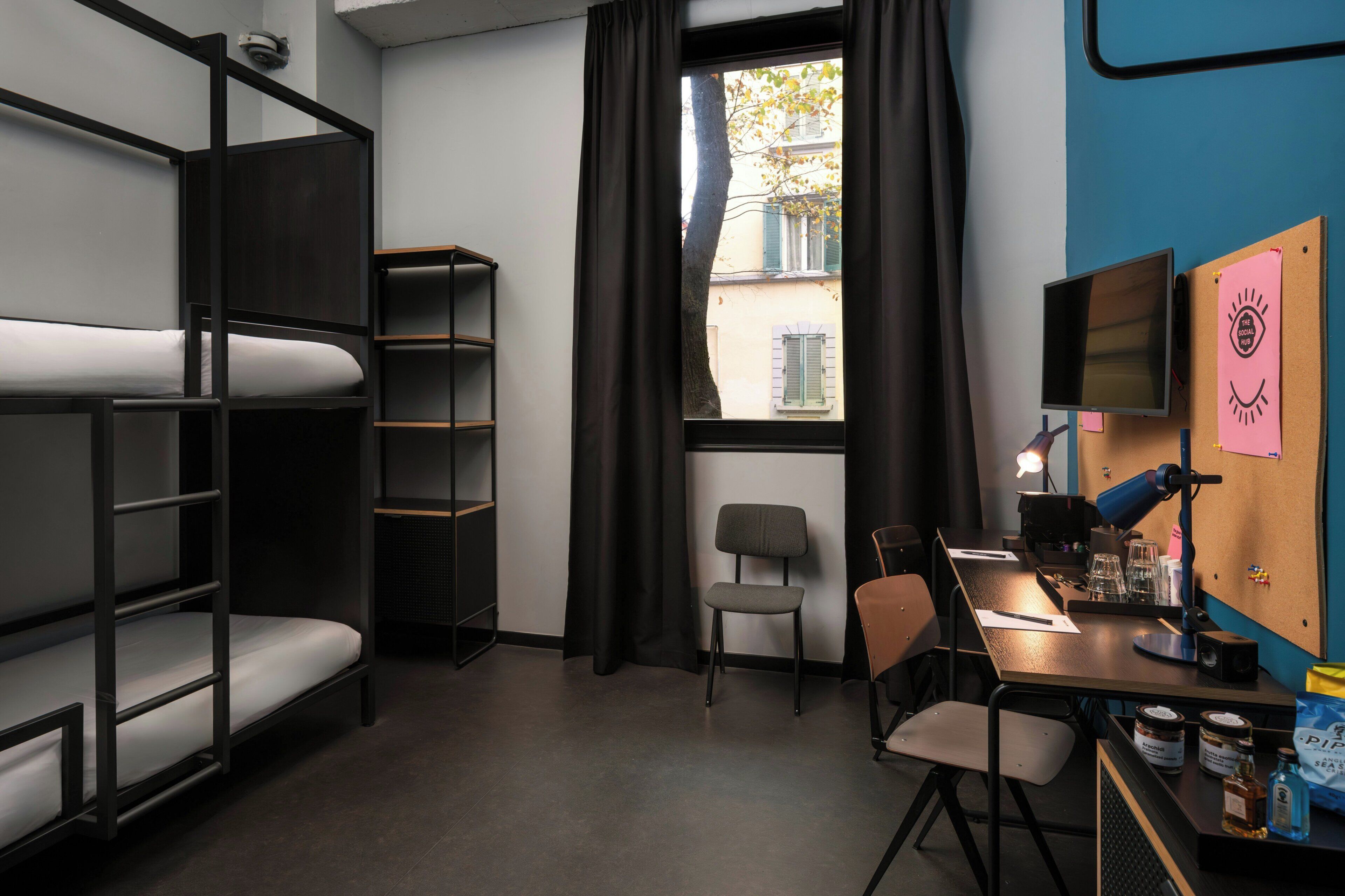 Une chambre de type dortoir, avec des lits superposés, un bureau avec un ordinateur, une chaise et une fenêtre avec des rideaux.