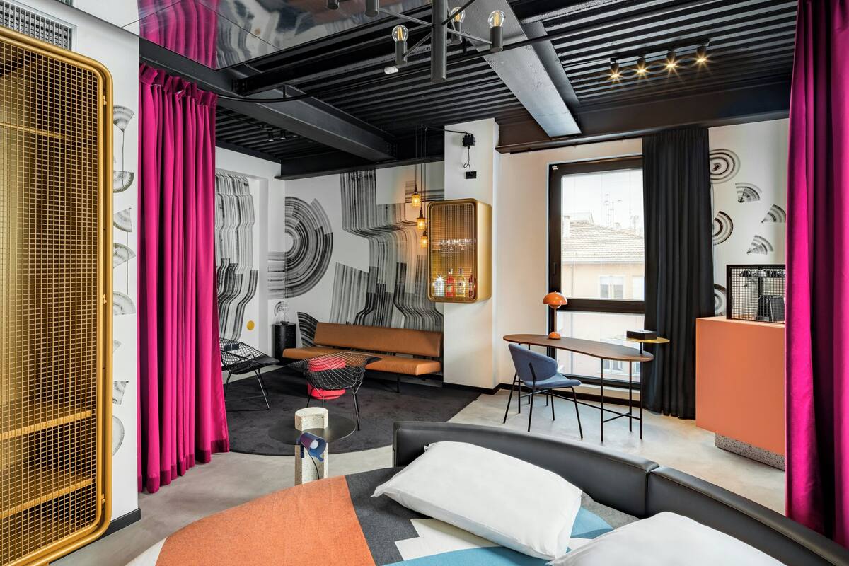 Une chambre d’hôtel moderne équipée d’un lit, d’un bureau, d’une chaise, d’un canapé et d’une grande fenêtre.