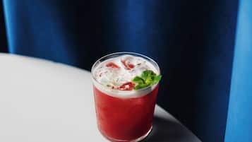 A glass of red beverage with ice and a mint garnish on a white surface.