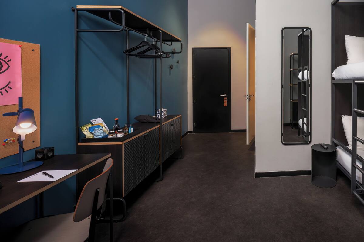 Une chambre d’hôtel de taille réduite, équipée d’un bureau, d’une chaise et d’un lit avec une tête de lit.