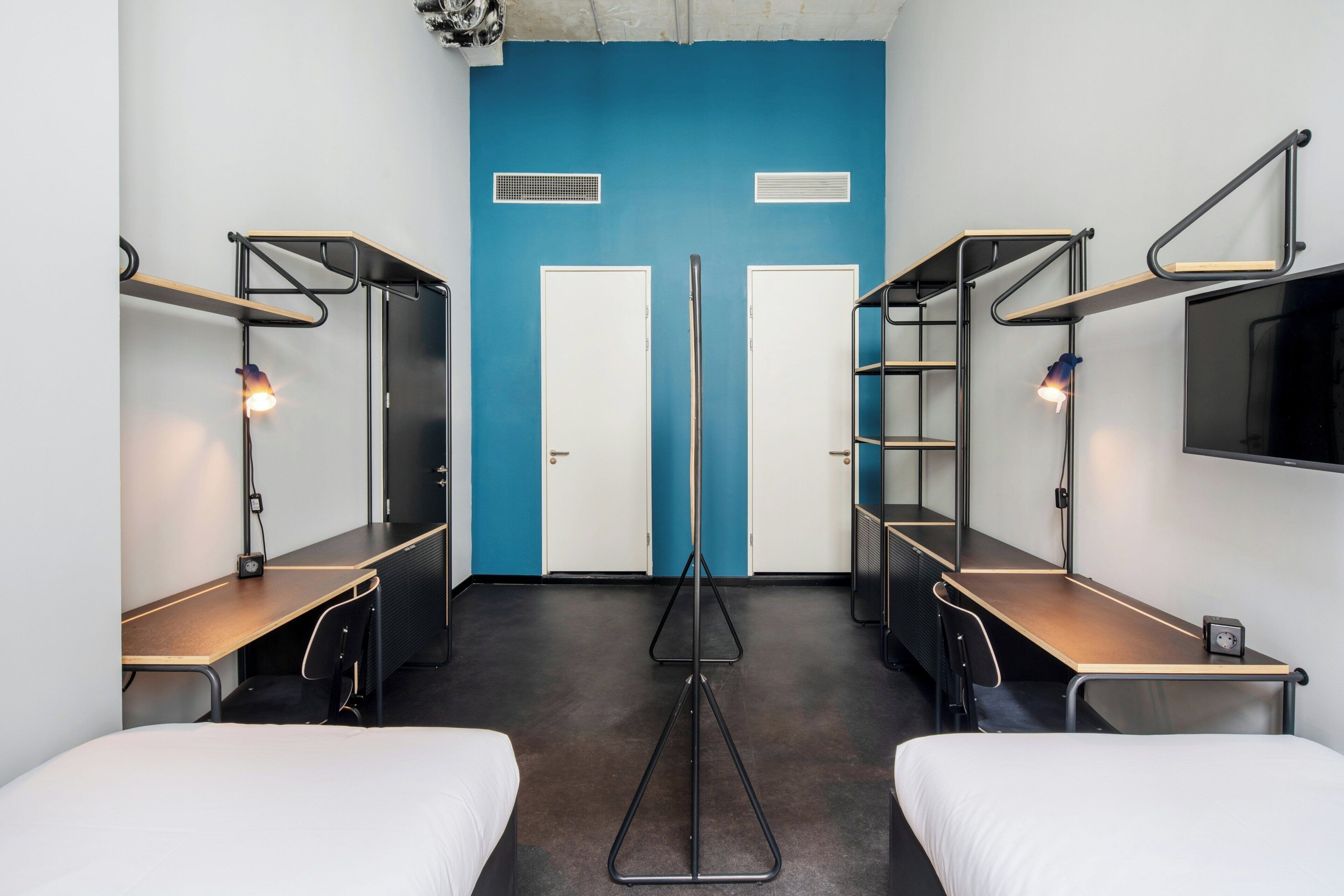 A room with bunk beds, a desk, a chair, a TV, and a blue accent wall.