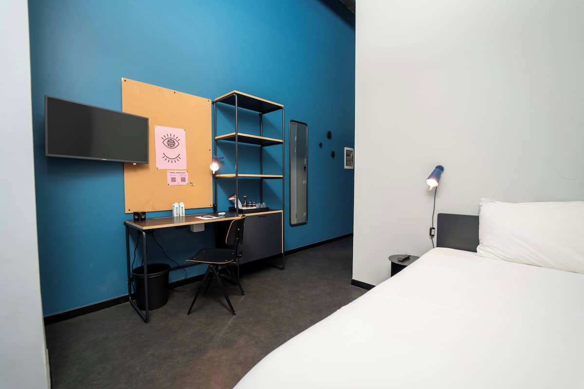 Une chambre d’hôtel comprenant un lit, un bureau avec une chaise, une télévision et une étagère.