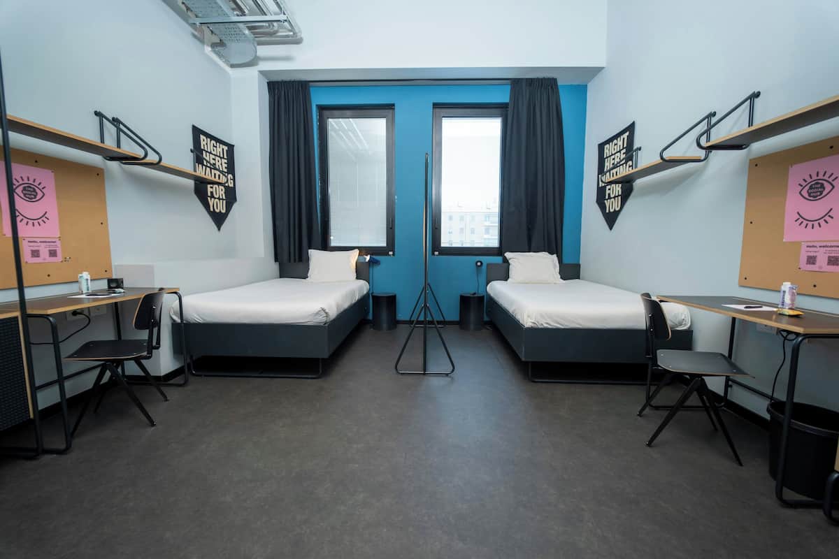 Une chambre double avec deux lits, un bureau, des chaises, une porte bleue et des décorations murales noires.