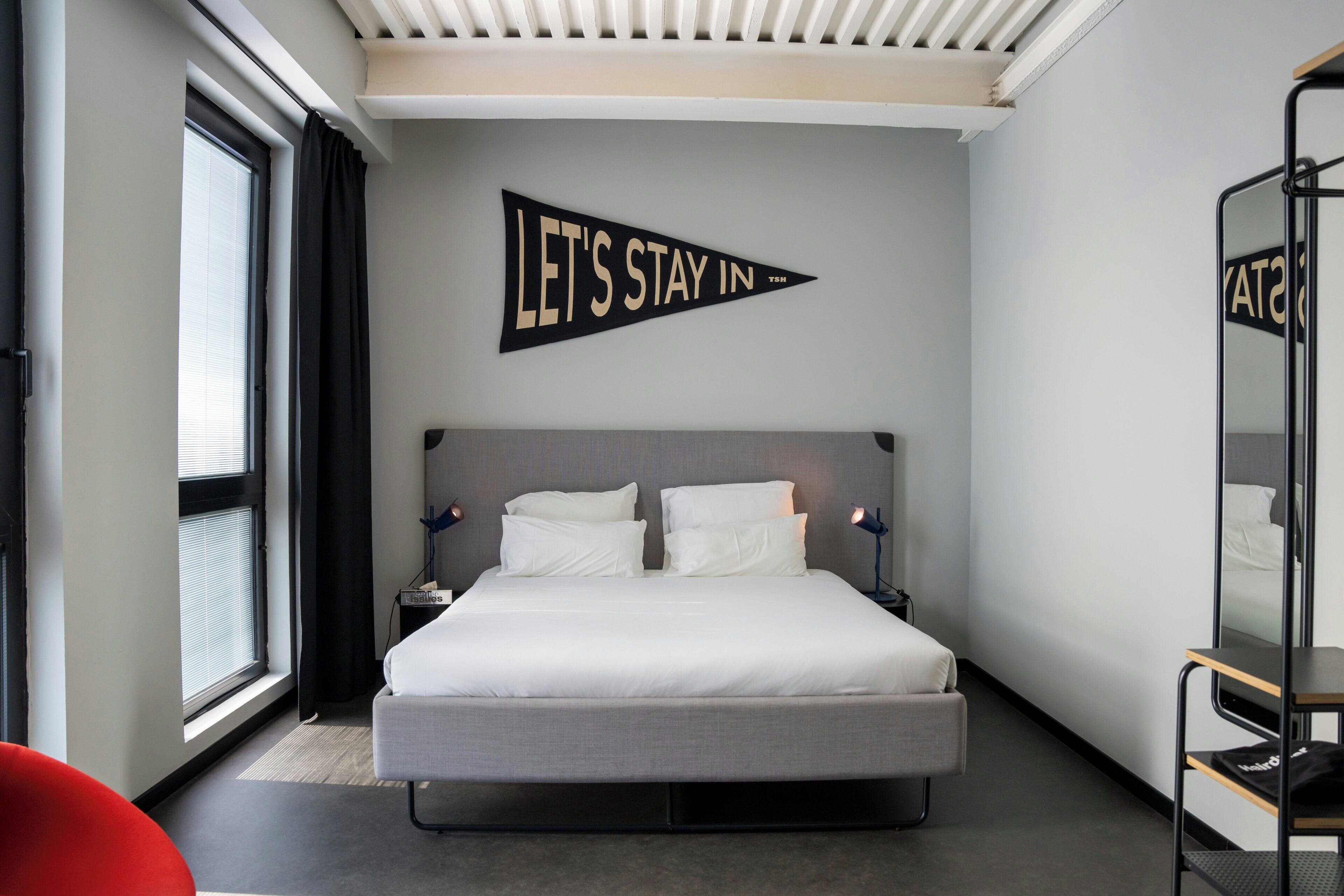 Habitación de hotel moderna con una cama grande, una mesita de noche, un espejo y una ventana con cortinas.