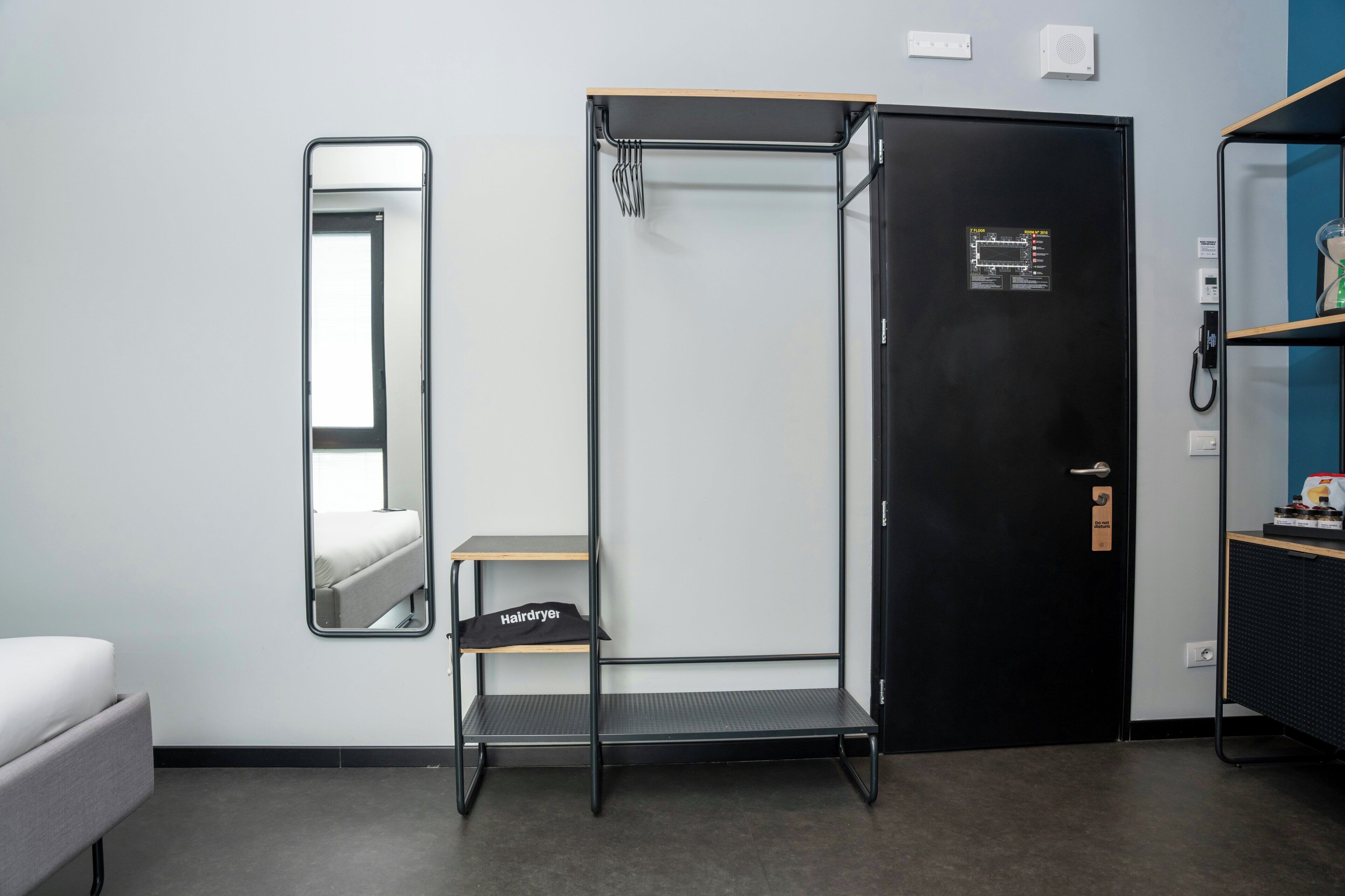 Ein kleines Zimmer mit Bett, Spiegel, schwarzem Kleiderschrank, Ablagefläche und Heizung.
