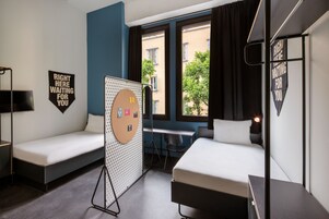 A hotel room with two single beds, a desk, and a chair. There are two signs on the walls, one reads "RIGHT HERE WAITING FOR YOU" and the other "RIGHT HERE WAITING FOR YOU".