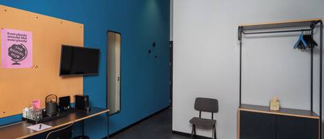 Una habitación moderna con una pared azul de acento, un televisor montado, un escritorio con silla, un estante pequeño y un perchero.