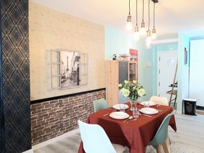 Un coin repas avec un mur en briques, un tableau encadré, un meuble en bois et une table dressée pour quatre personnes.