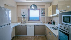 A modern kitchen with a built-in dishwasher, a gas stove, and a large window overlooking the sea. - Lara Park Suites (Antalya)