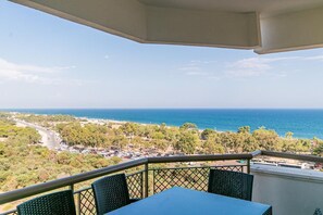 A balcony with a table and chairs overlooking a coastal area with a road and greenery. - Lara Park Suites (Antalya)