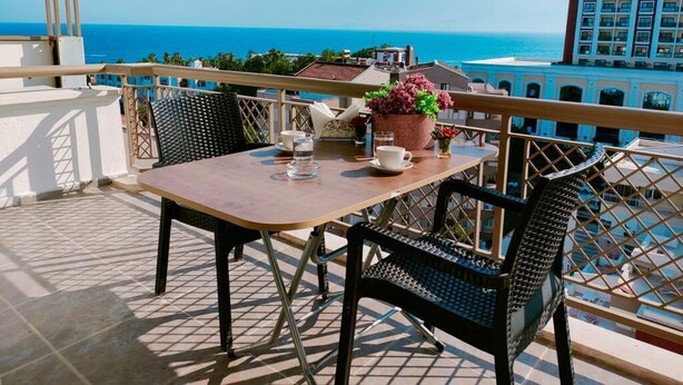 A balcony with a table and chairs, overlooking a coastal view with buildings in the background. - Lara Park Suites (Antalya)