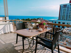 A balcony with a table and chairs, overlooking a coastal view with buildings in the background. - Lara Park Suites (Antalya)