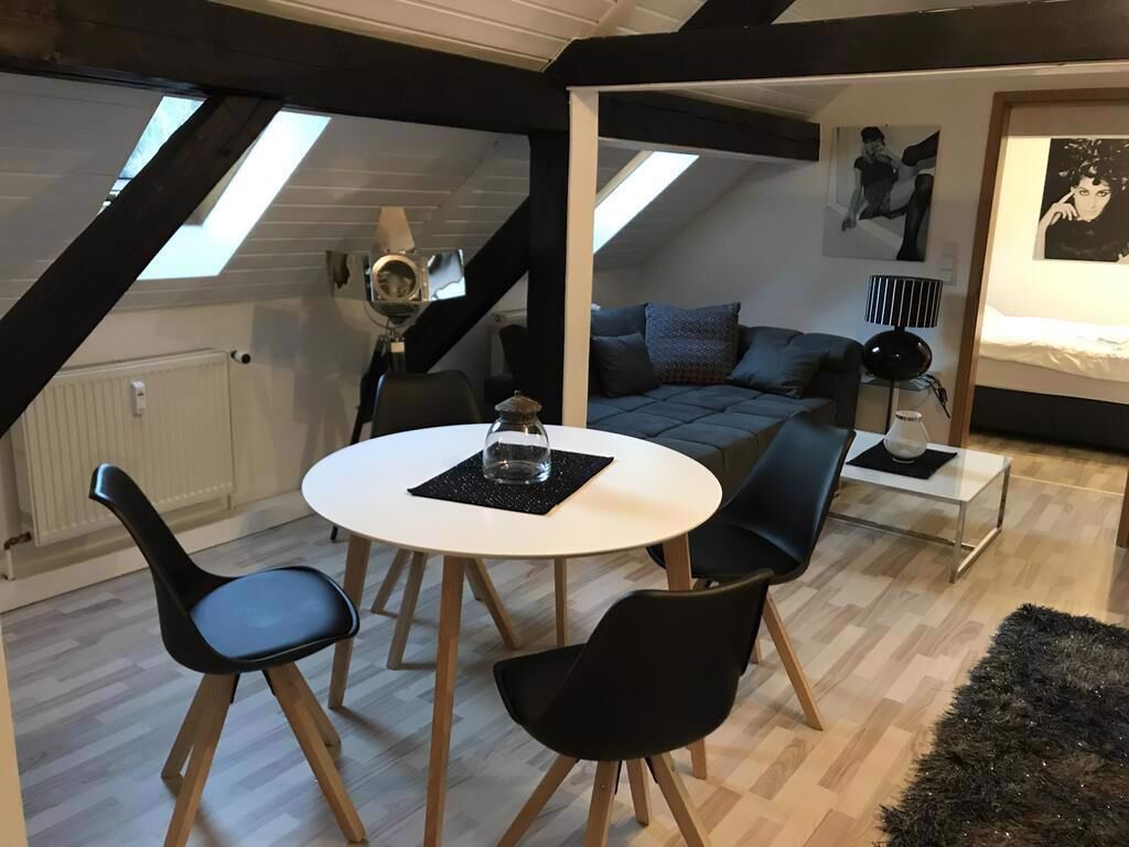 Ein modernes Loft-Schlafzimmer mit Oberlicht, einer Couch, einem Esstisch mit Stühlen und einem schwarzen Teppich.