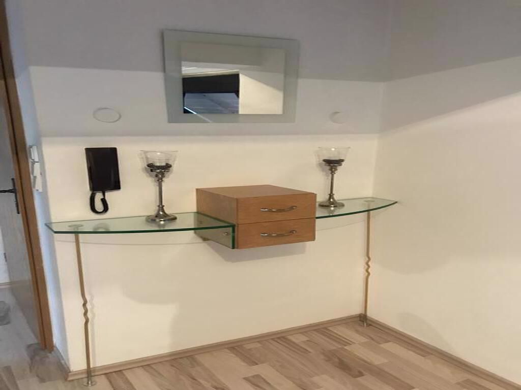 A small room with a glass-top desk, a wooden cabinet, a mirror, and two lamps.