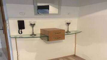A small room with a glass-top desk, a wooden cabinet, a mirror, and two lamps.