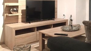 Moderni olohuone, jossa on seinälle asennettu taulutelevisio, lasinen sohvapöytä, musta sohva ja koristeellinen metalliveistos.