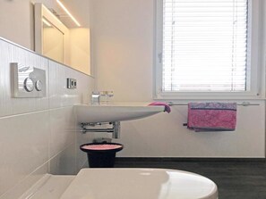 Ein modernes Badezimmer mit einem weißen Waschbecken, einem Spiegel und einem Fenster mit Jalousien.