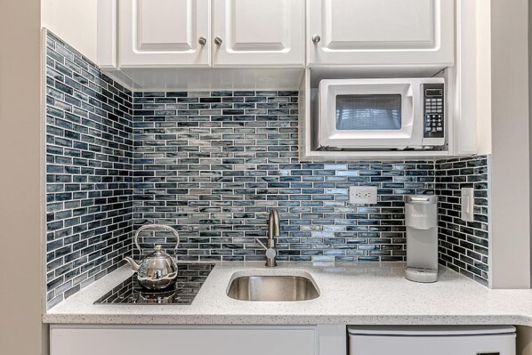 A kitchen with white cabinets, a microwave, a kettle, and a coffee maker.