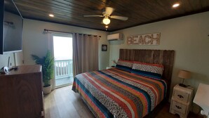 Un dormitorio con una cama grande, un ventilador de techo, un equipo de aire acondicionado y vista a la playa a través de un ventanal corredero.