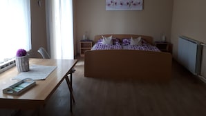 Une chambre à coucher avec un lit en bois, une table de chevet, une chaise, une fenêtre avec des rideaux et une œuvre d’art accrochée au mur.