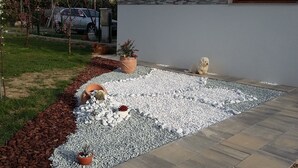 Un jardin avec un chemin de gravier, des plantes en pot et un chien.