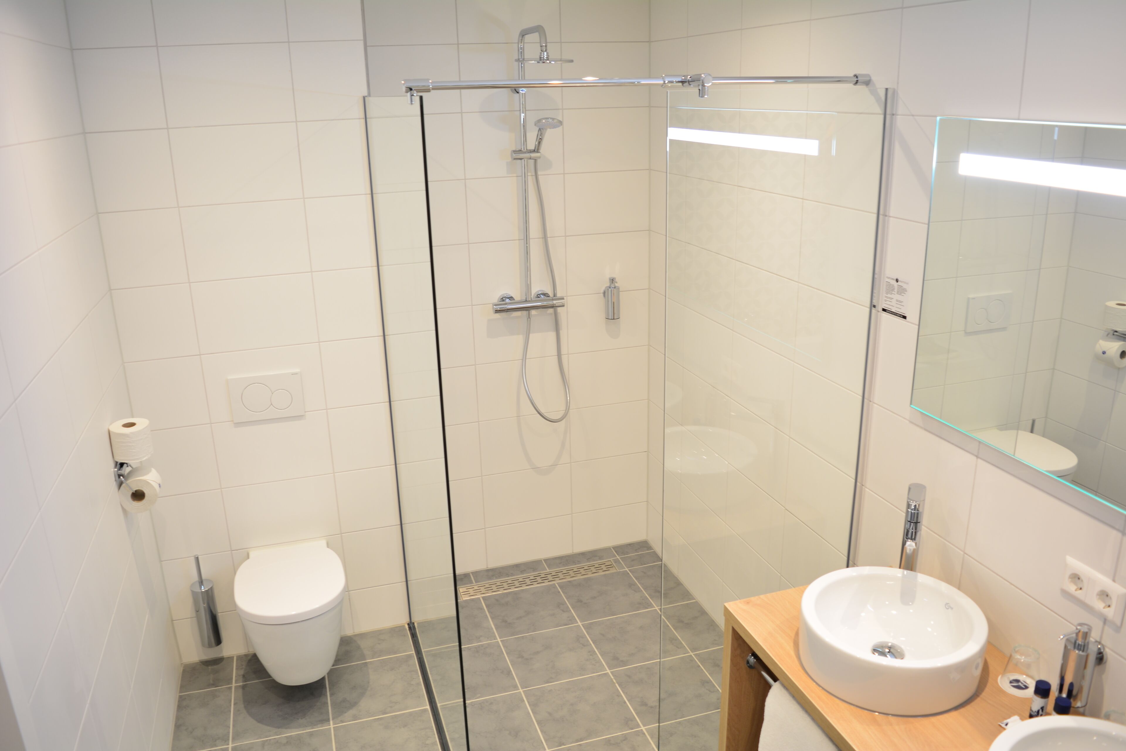 Un baño moderno con ducha de vidrio, inodoro y lavamanos con espejo.