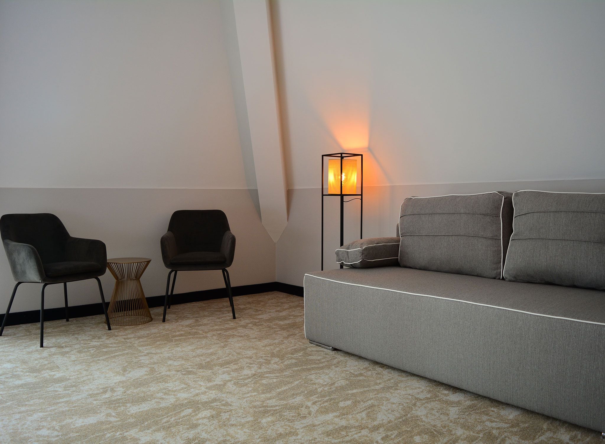Una sala de estar minimalista con un sofá gris, dos sillas negras, una mesita de madera y una lámpara de pie.