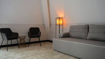 Una sala de estar minimalista con un sofá gris, dos sillas negras, una mesita de madera y una lámpara de pie.
