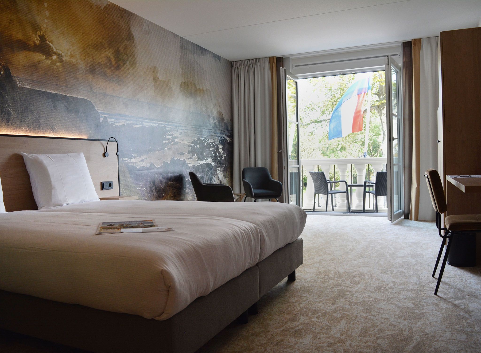 Ein Hotelzimmer mit einem großen Bett, Blick ins Freie und einem Balkon mit Sitzgelegenheiten.