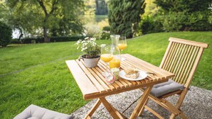 Une table en bois, installée à l’extérieur, sur laquelle on a posé une plante en pot, une carafe en verre et un verre de jus d’orange.
