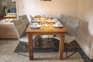 A dining table set with white plates, bowls, and glasses, surrounded by grey upholstered chairs.