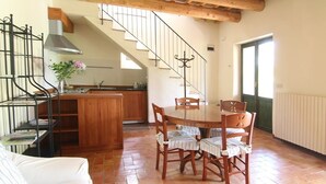 Un comedor con una mesa y sillas de madera, una escalera y una cocina al fondo.