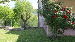Un jardín con muro de ladrillo, cerca metálica y un árbol.