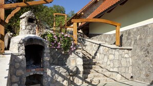 Un espacio al aire libre de piedra con un horno rústico de piedra, vigas de madera y una pared de piedra.