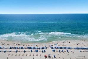 A beach with rows of blue umbrellas and sun loungers, a volleyball net, and a clear view of the ocean. - BEAUTIFUL BEACHFRONT! SPACIOUS COASTAL RETREAT! 1 MILE E OF PIER PARK!BCH SRVC INCL!!! (Panama City Beach)