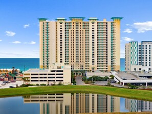 A high-rise hotel with multiple floors, a parking area, and a body of water reflecting the building.