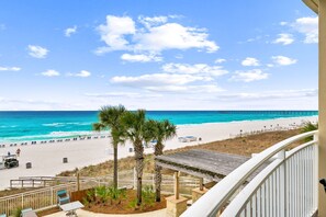 A beach view with a wooden deck, palm trees, and a pier in the distance.