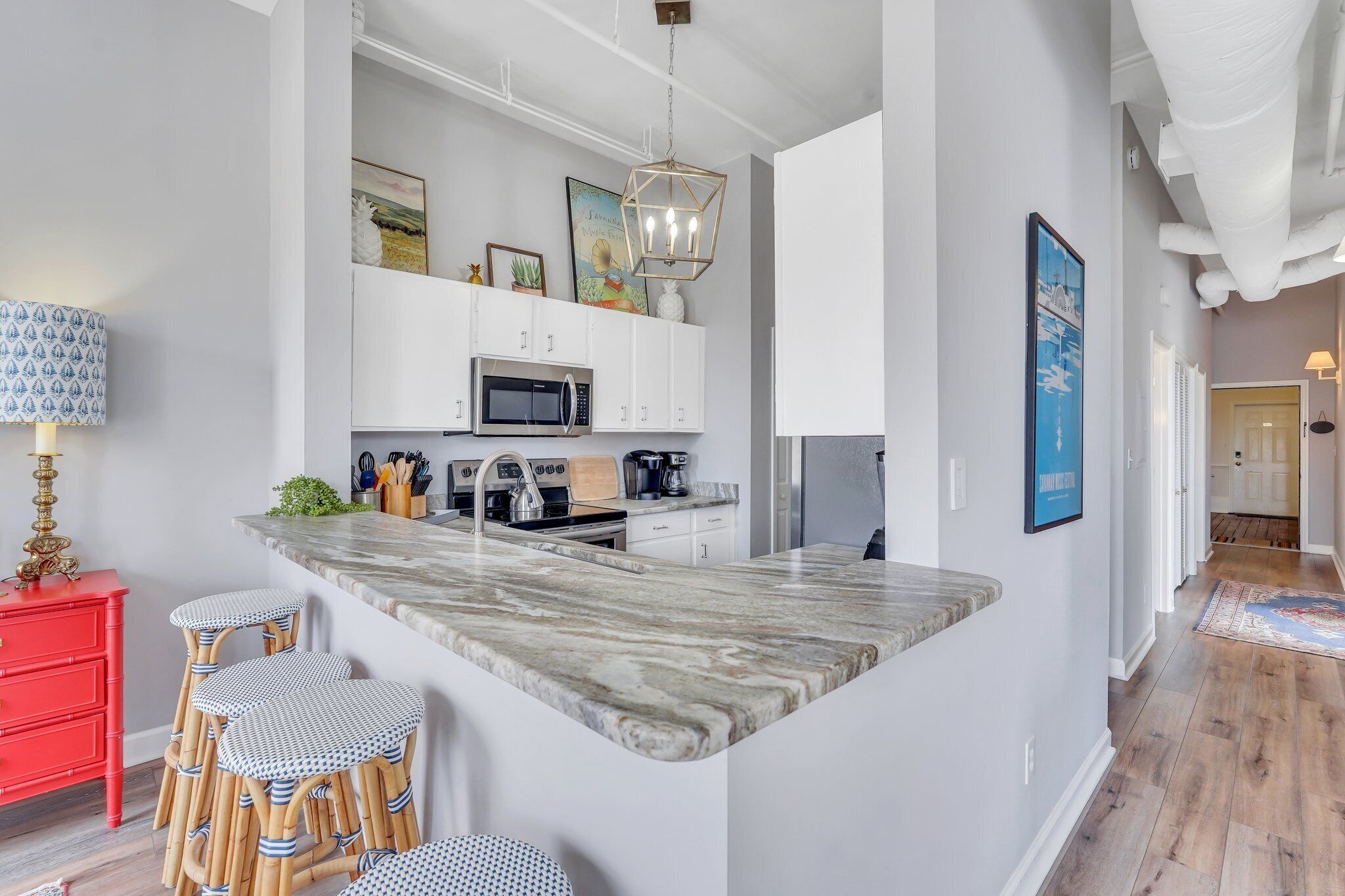A modern kitchen with a marble island, white cabinets, and a red sideboard.