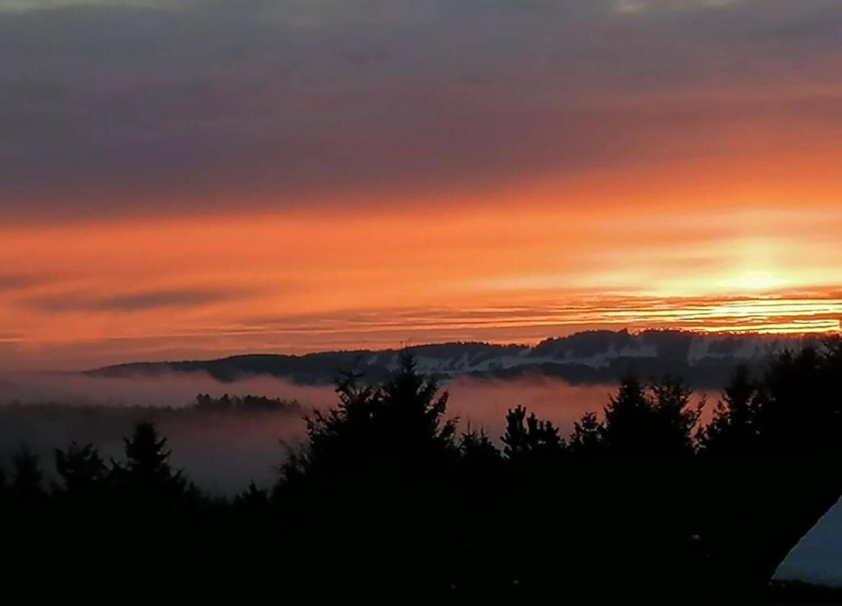 Un lever de soleil sur un paysage montagneux, avec une forêt au premier plan.